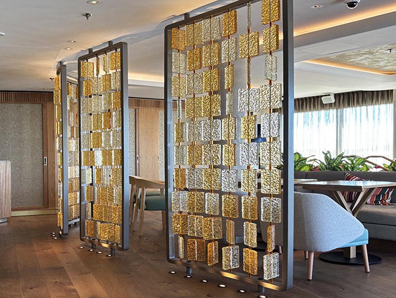 Freestanding cast glass screens with amber and clear textured tiles dividing the restaurant at The BoTree hotel, London